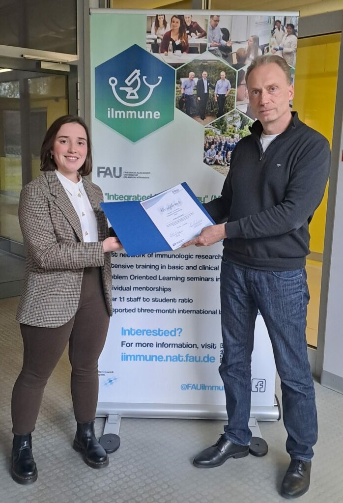 Chiara Hornung and Prof. Nimmerjahn stand in front of the iImmune poster showing the iImmune certificate